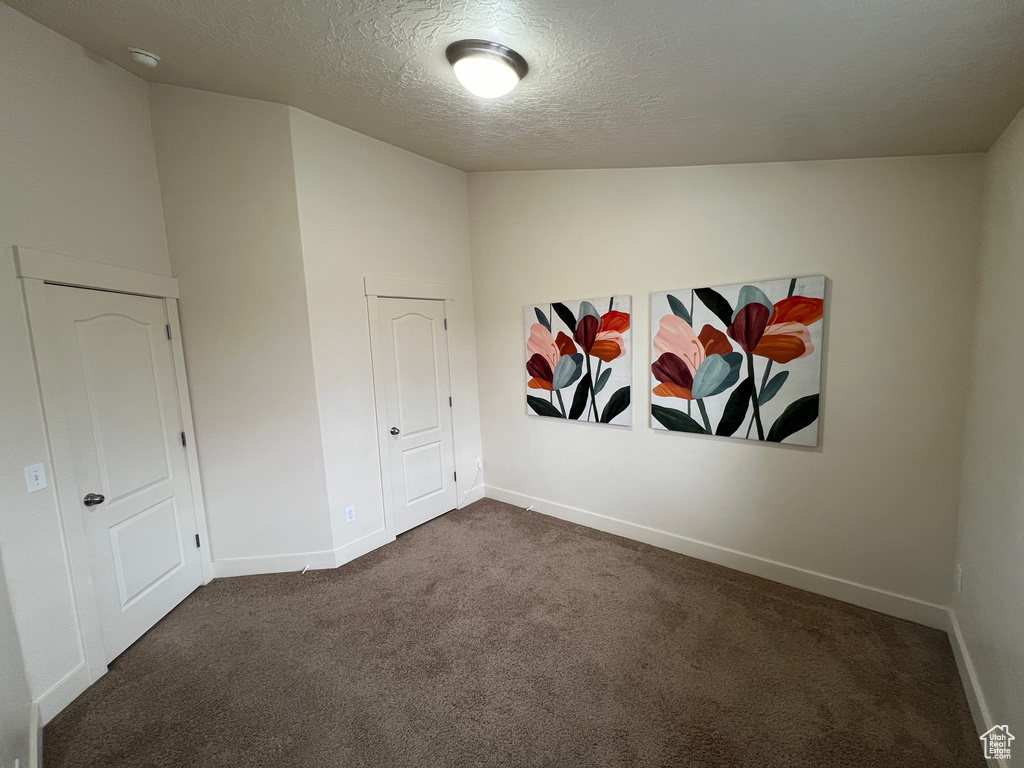 Empty room featuring dark colored carpet, a textured ceiling, and baseboards