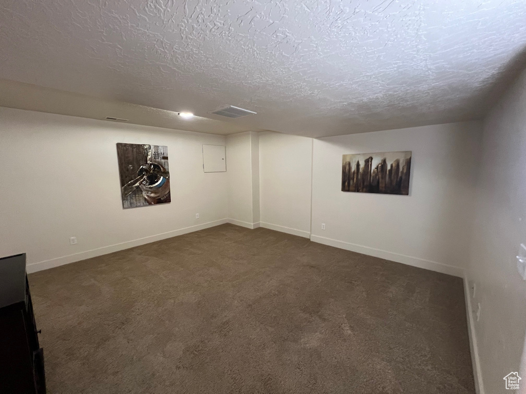 Finished basement featuring dark carpet, a textured ceiling, and baseboards