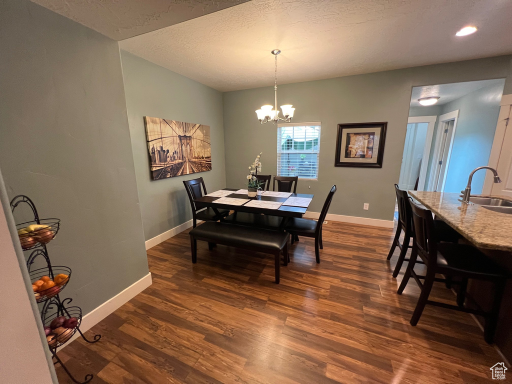 Dining area featuring dark wood-type flooring, a textured ceiling, baseboards, and an inviting chandelier