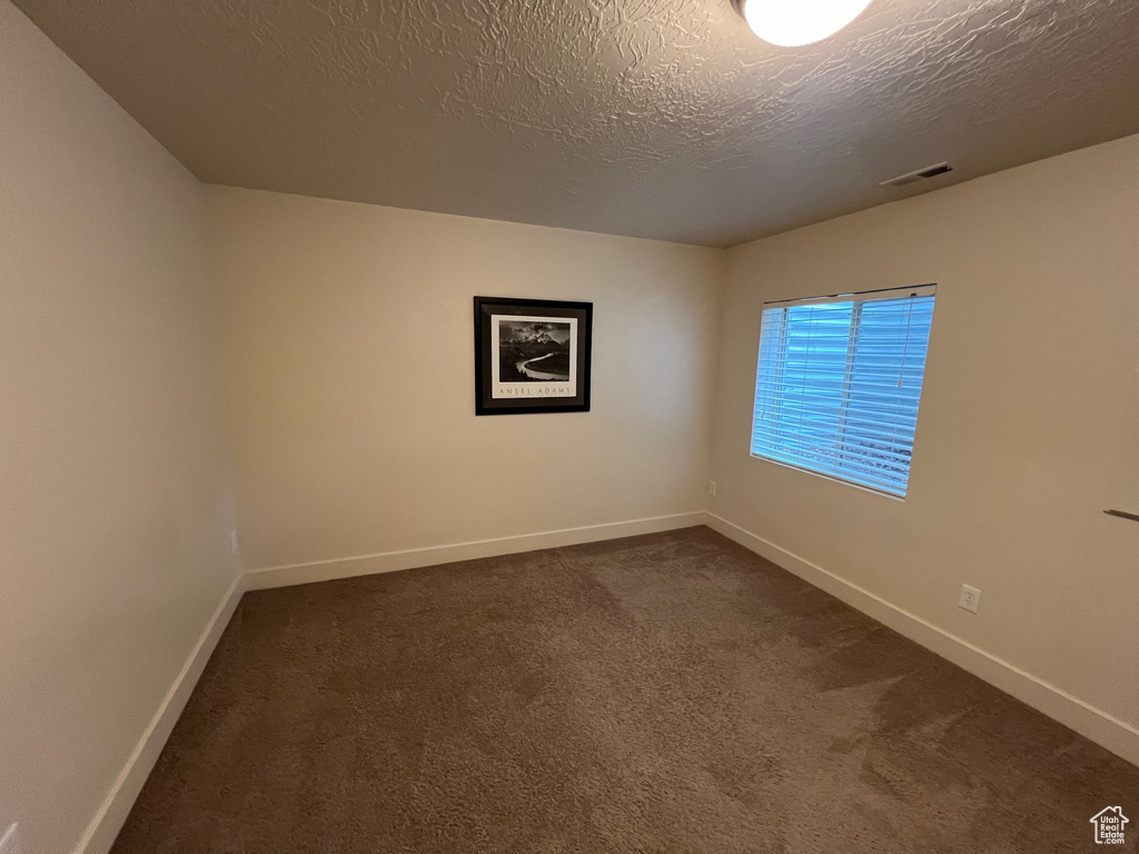 Spare room featuring baseboards, dark colored carpet, a textured ceiling, and visible vents