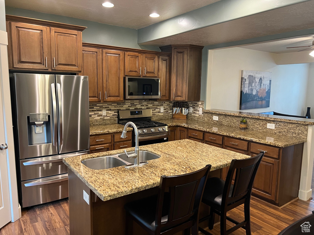 Kitchen with decorative backsplash, a peninsula, dark wood-style floors, a sink, and stainless steel appliances