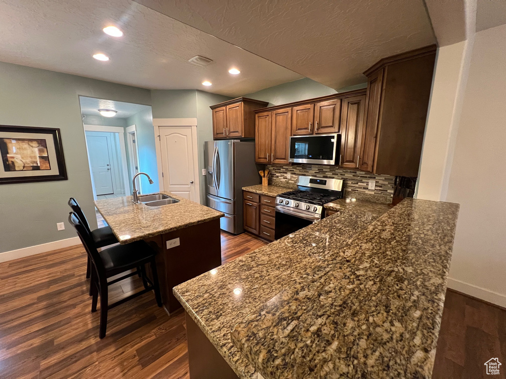 Kitchen with dark wood-style flooring, appliances with stainless steel finishes, a sink, a breakfast bar area, and baseboards