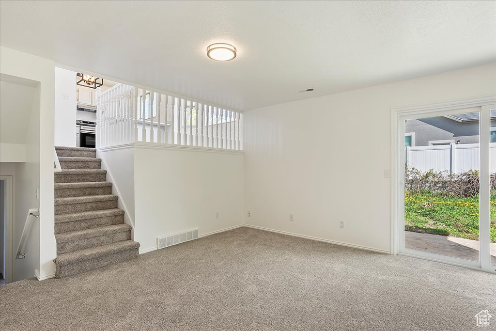Unfurnished living room featuring stairway, a chandelier, carpet, baseboards, and visible vents