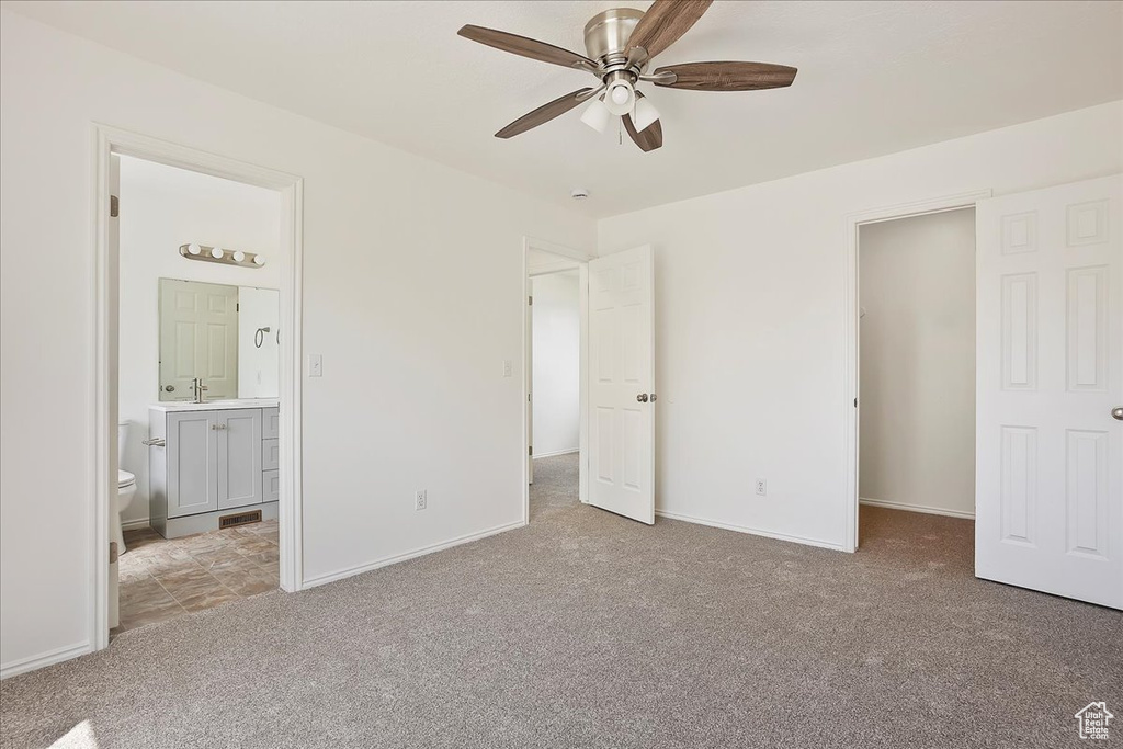 Unfurnished bedroom featuring a walk in closet, baseboards, carpet floors, and ensuite bath