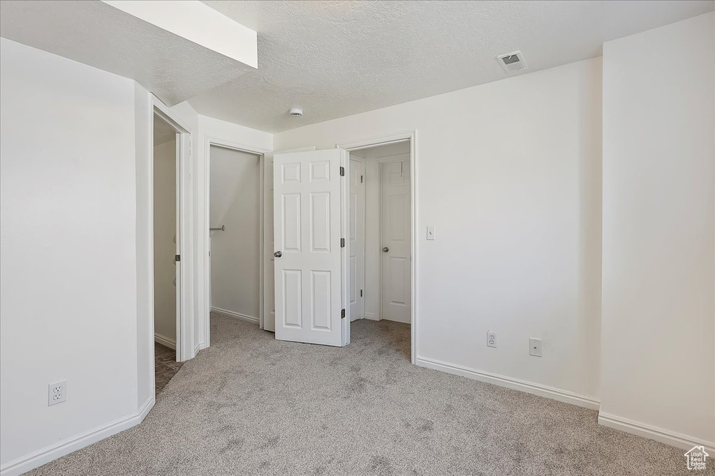 Unfurnished bedroom with a textured ceiling, visible vents, carpet flooring, and baseboards