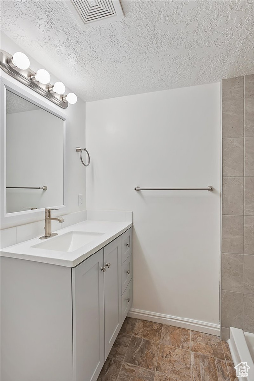 Bathroom with baseboards, visible vents, a textured ceiling, and vanity
