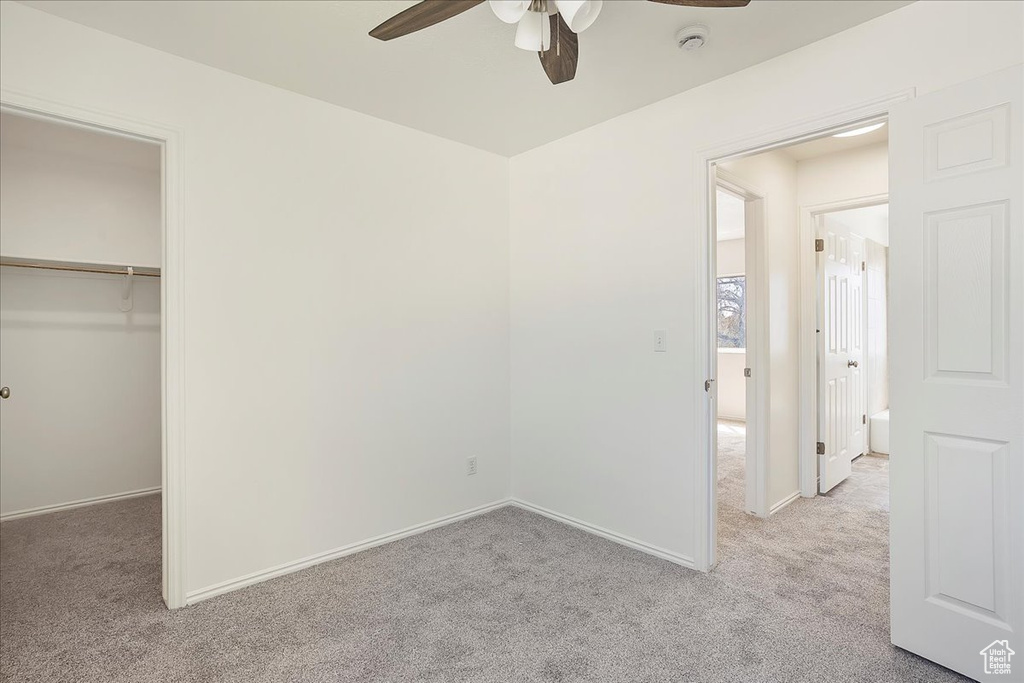 Unfurnished bedroom featuring a walk in closet, a ceiling fan, baseboards, and light carpet