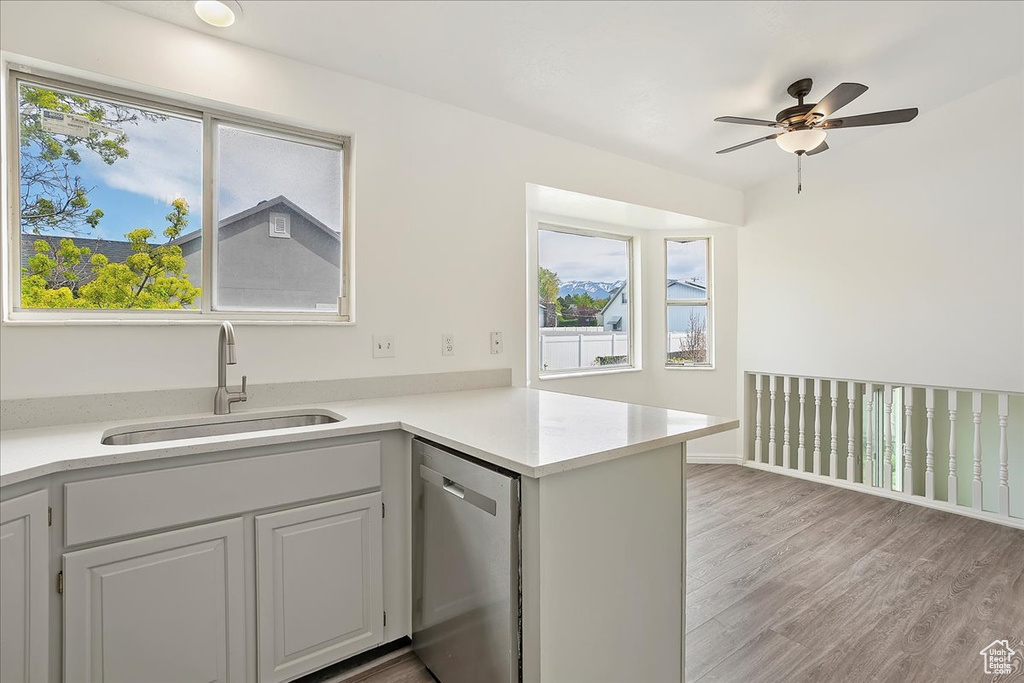 Kitchen with light wood-style floors, light countertops, ceiling fan, dishwasher, and a sink