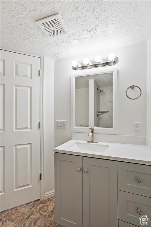 Bathroom with a textured ceiling, visible vents, and vanity