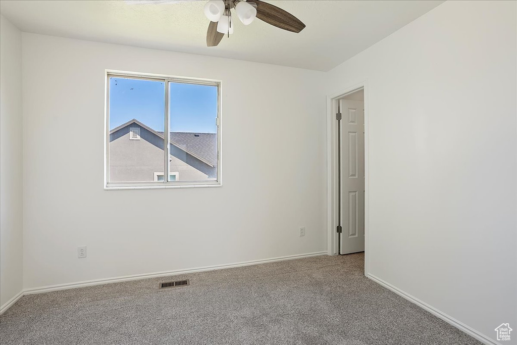 Carpeted empty room with baseboards, visible vents, and a ceiling fan