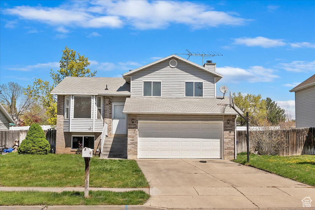 Tri-level home with a front yard, fence, a garage, and brick siding