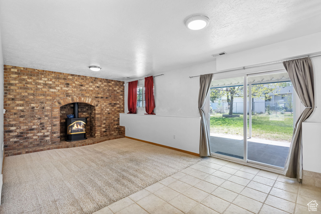 Unfurnished living room with a textured ceiling, a wood stove, visible vents, baseboards, and tile patterned flooring