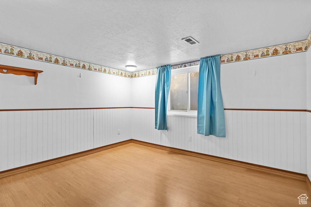 Empty room with a textured ceiling, visible vents, wood finished floors, and baseboards