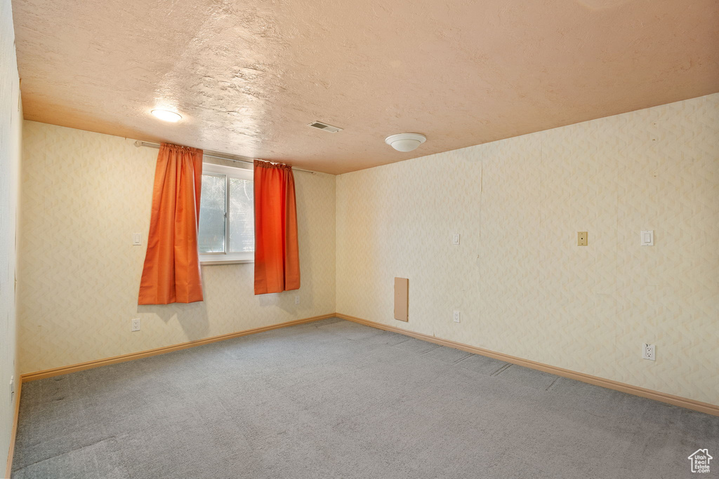 Carpeted spare room with a textured ceiling, visible vents, and baseboards