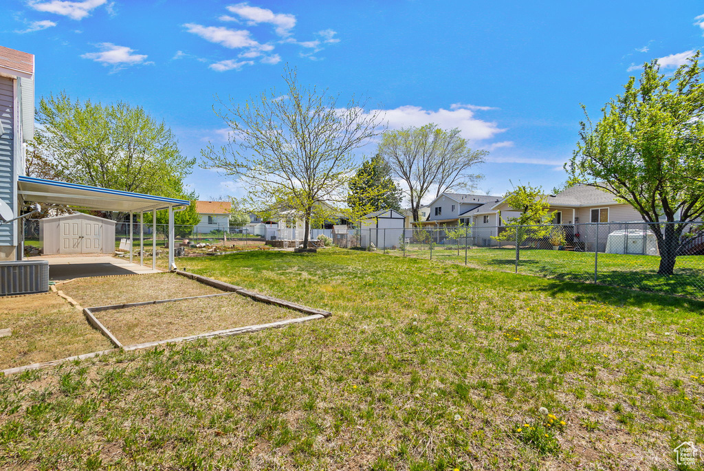 View of yard featuring an outdoor structure, fence, a storage shed, a residential view, and central AC unit