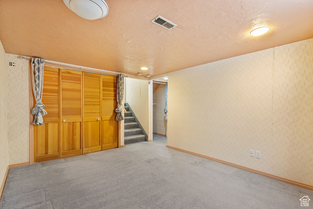Finished below grade area featuring stairs, carpet flooring, a textured ceiling, and visible vents