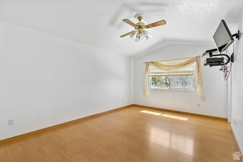 Empty room featuring a ceiling fan, baseboards, vaulted ceiling, and light wood-style floors
