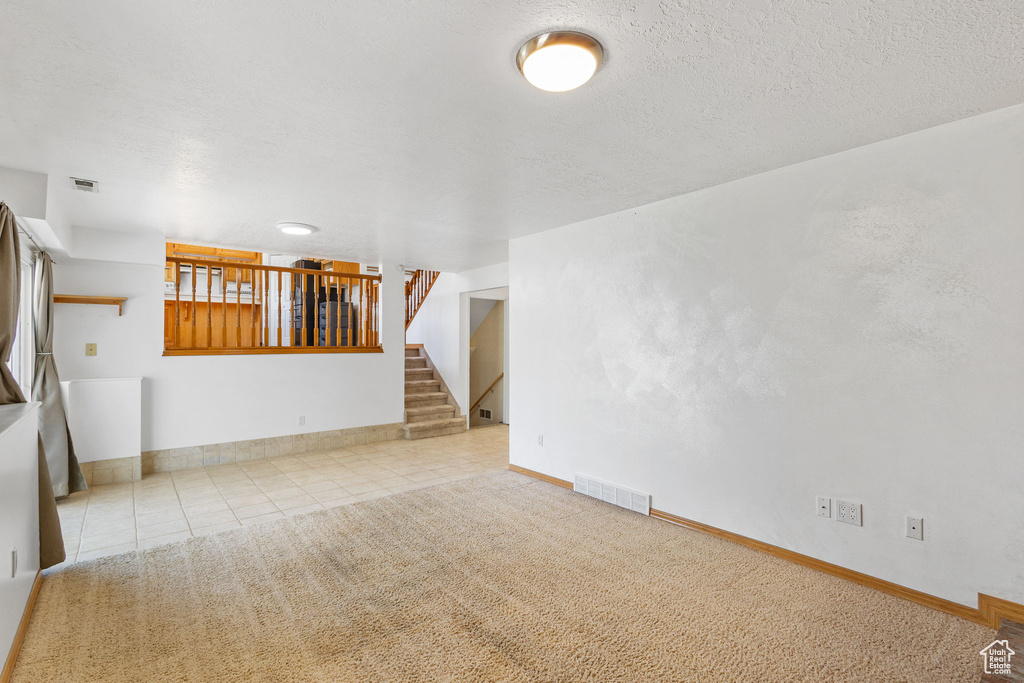 Unfurnished living room with tile patterned floors, stairway, visible vents, and a textured ceiling