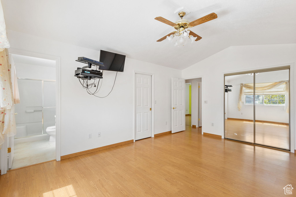 Unfurnished bedroom featuring connected bathroom, two closets, vaulted ceiling, light wood-style flooring, and baseboards