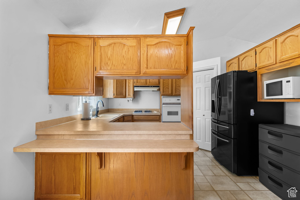 Kitchen featuring a sink, under cabinet range hood, a peninsula, white appliances, and lofted ceiling