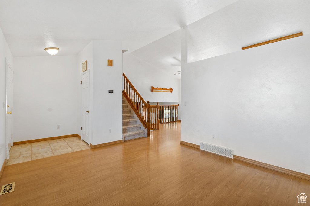 Empty room with baseboards, visible vents, stairs, and light wood-style floors
