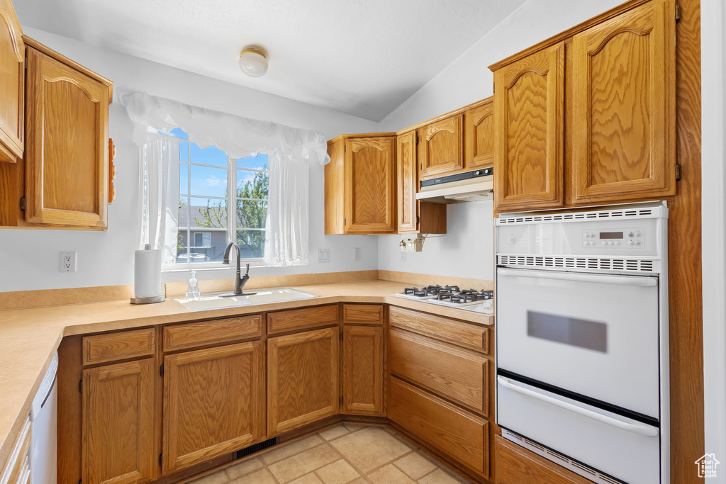 Kitchen featuring a sink, light countertops, under cabinet range hood, a warming drawer, and white appliances