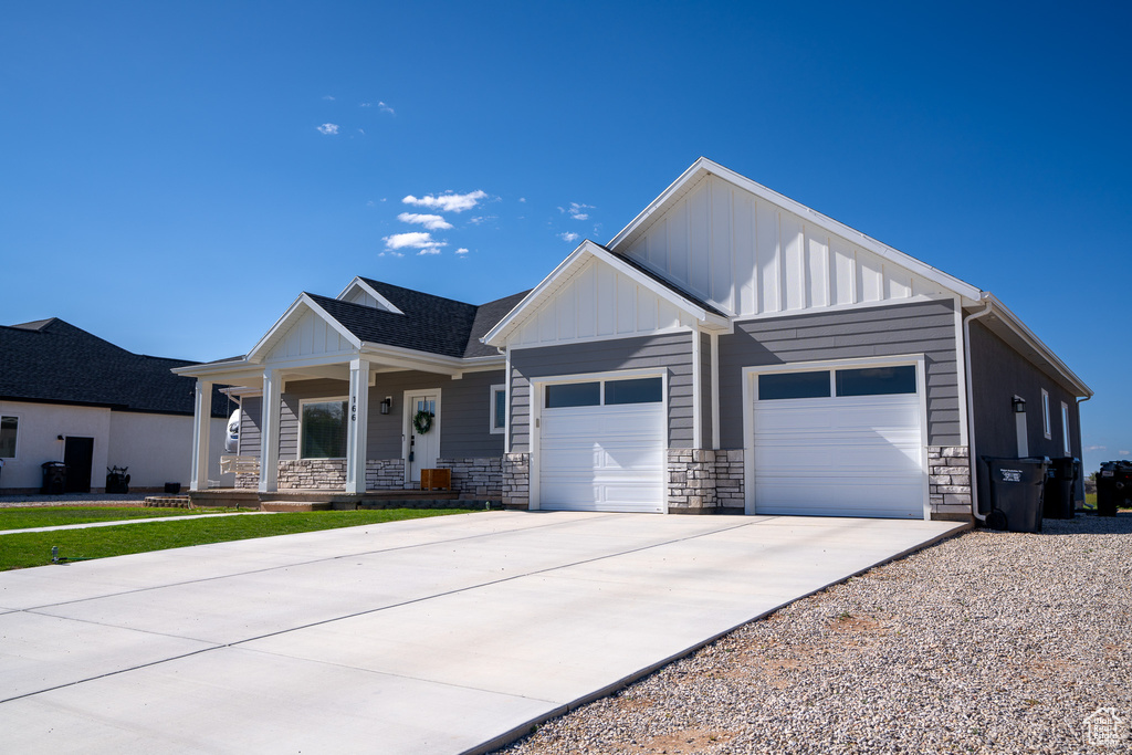 View of front of house featuring stone siding, a garage, board and batten siding, a porch, and driveway