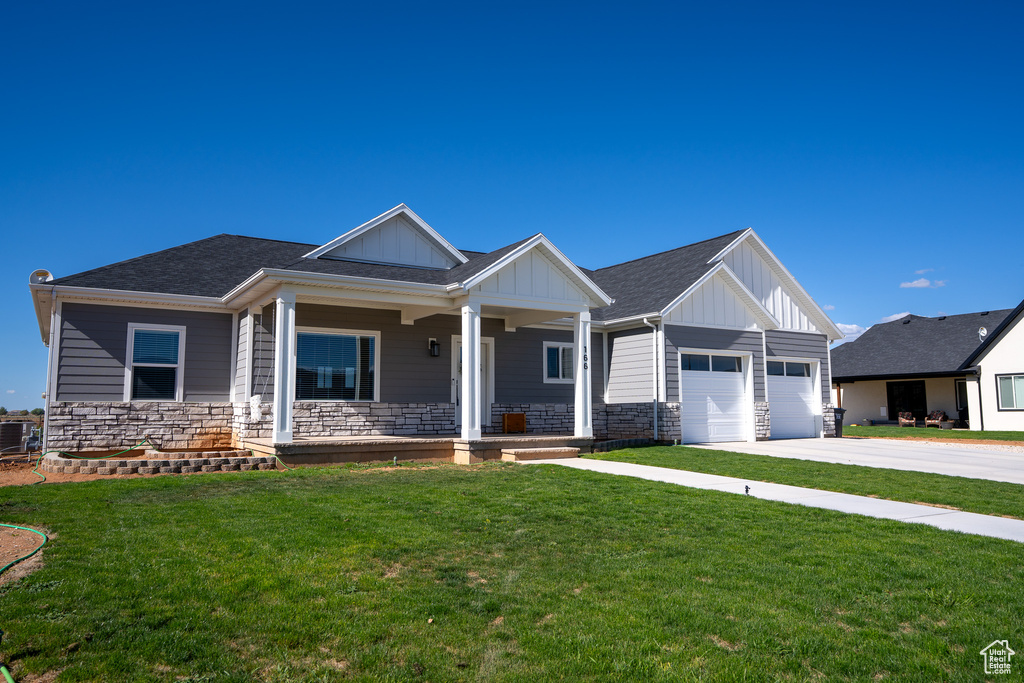 Craftsman house featuring board and batten siding, a front yard, covered porch, concrete driveway, and stone siding