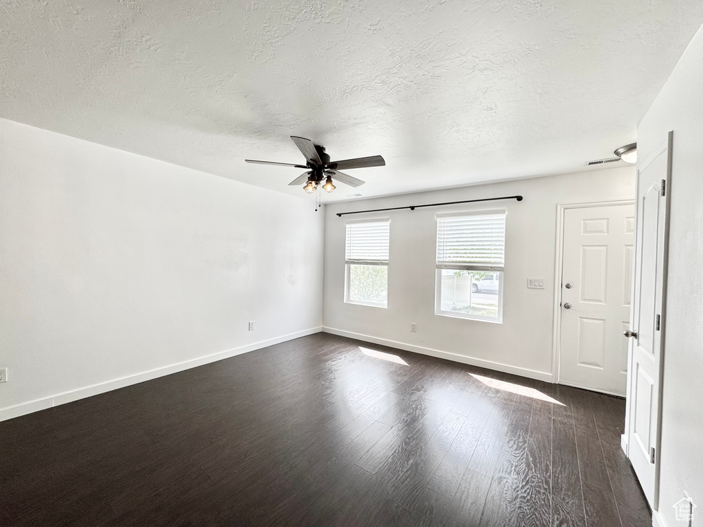 Empty room featuring dark wood-style floors, baseboards, ceiling fan, and a textured ceiling