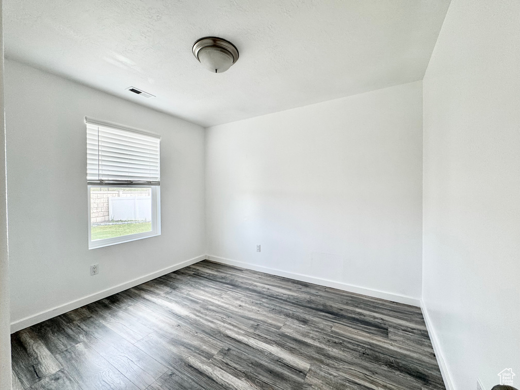 Empty room featuring dark wood-style flooring, visible vents, and baseboards