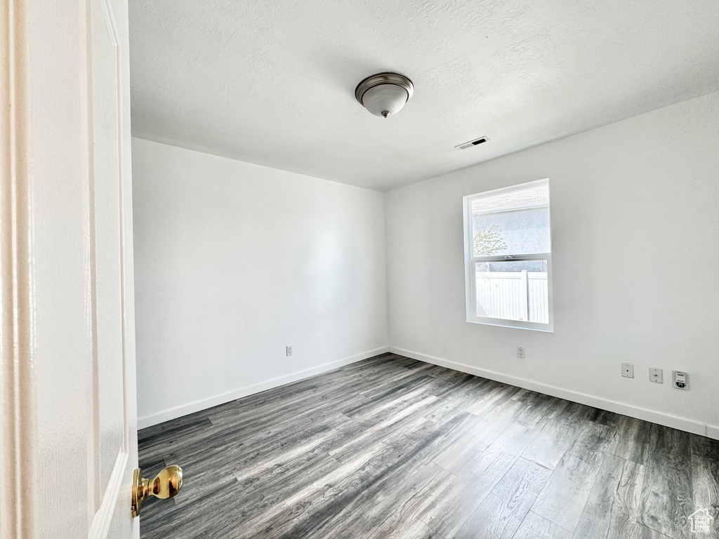 Spare room featuring dark wood-type flooring, visible vents, a textured ceiling, and baseboards