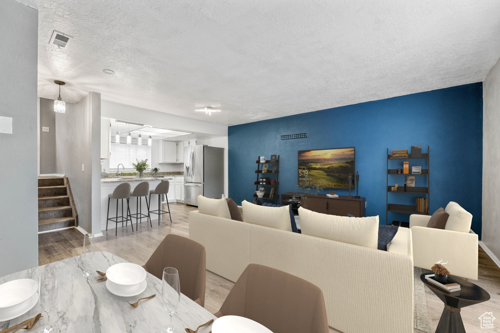 Living room featuring light wood-type flooring, a textured ceiling, baseboards, and stairs