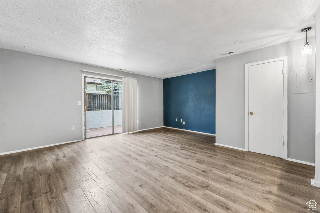 Empty room with a textured ceiling, wood finished floors, and baseboards