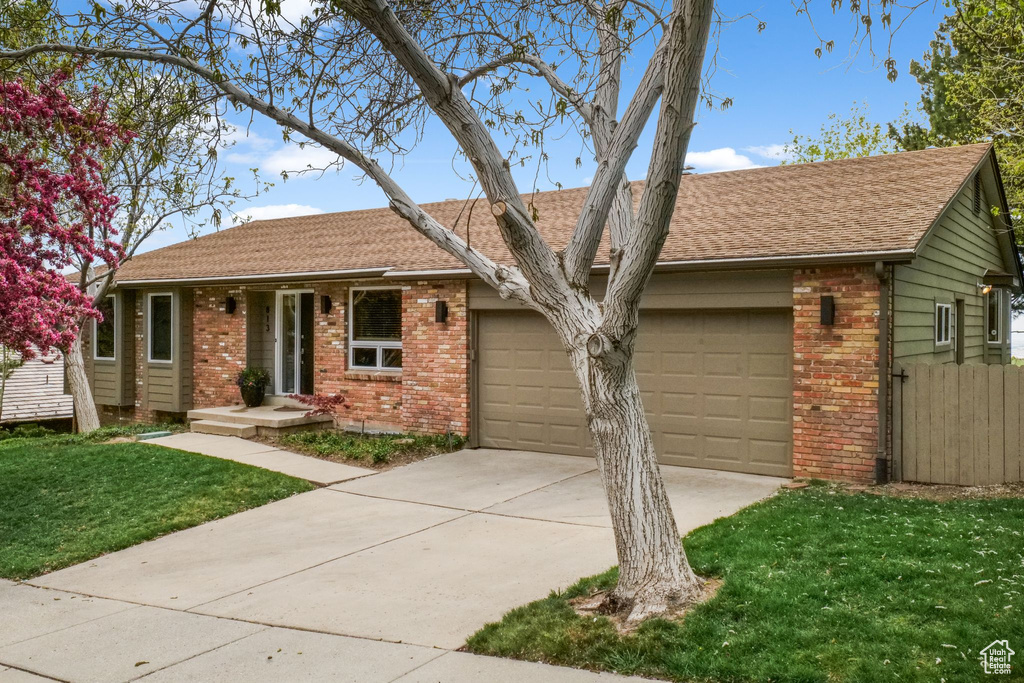 Single story home featuring brick siding, fence, a garage, driveway, and a front yard