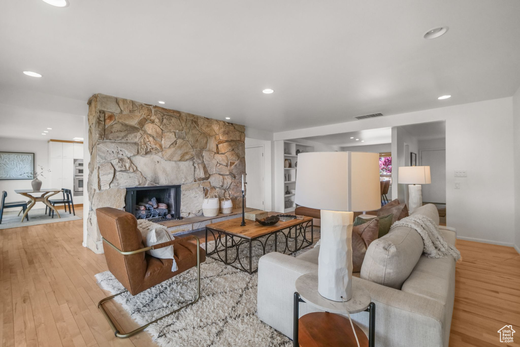 Living room with a fireplace, wood finished floors, recessed lighting, and visible vents