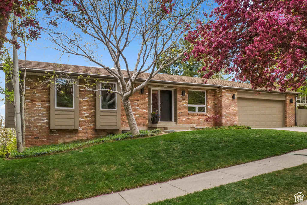 Ranch-style home with a front lawn, driveway, a garage, and brick siding