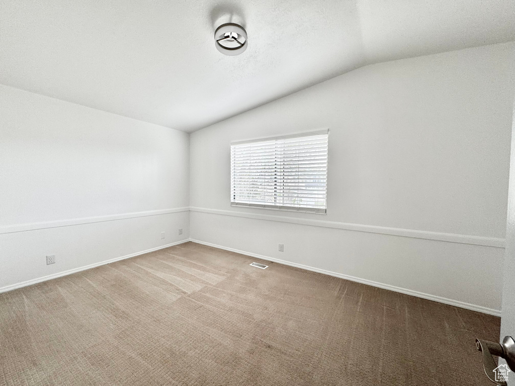 Carpeted empty room with lofted ceiling and baseboards