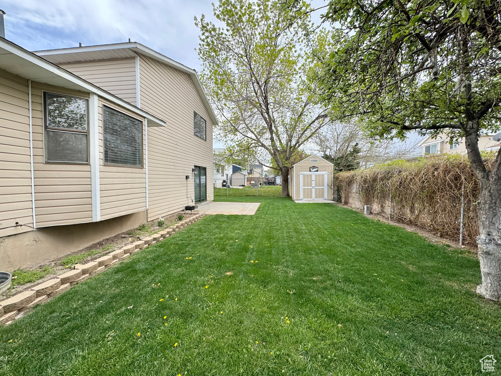 View of yard with fence, a shed, an outbuilding, and a patio area