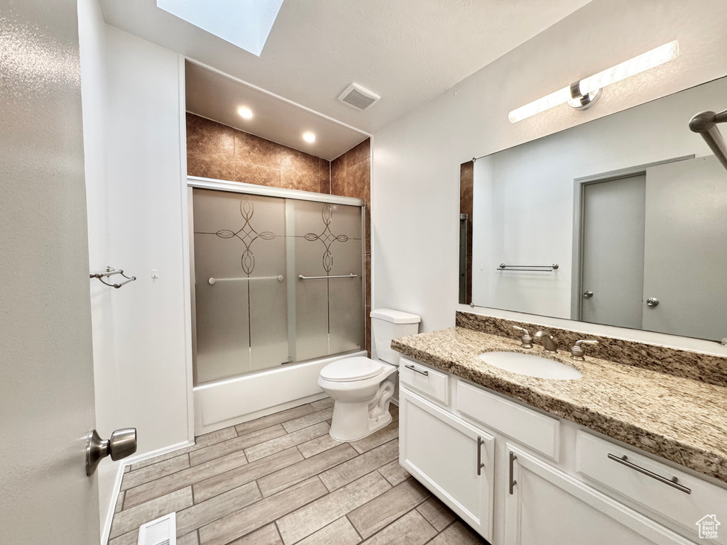 Full bathroom with a skylight, toilet, vanity, visible vents, and wood finish floors