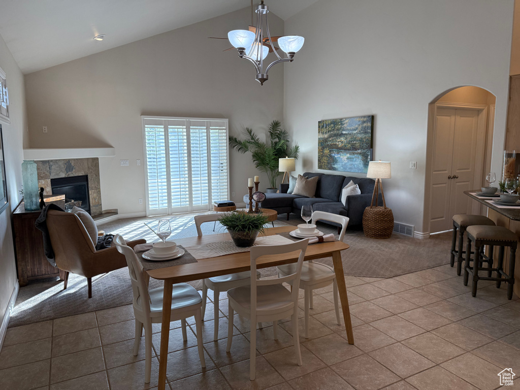 Dining area with high vaulted ceiling, a fireplace, arched walkways, light tile patterned flooring, and baseboards