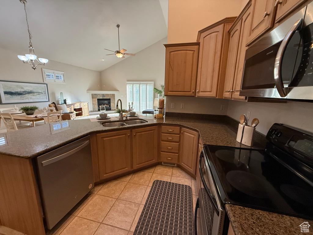 Kitchen featuring stainless steel appliances, a sink, a ceiling fan, a glass covered fireplace, and dark stone counters