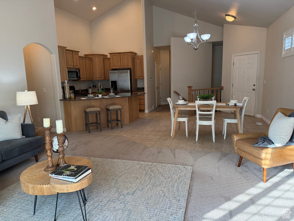 Living room with high vaulted ceiling, a chandelier, light colored carpet, arched walkways, and light tile patterned floors