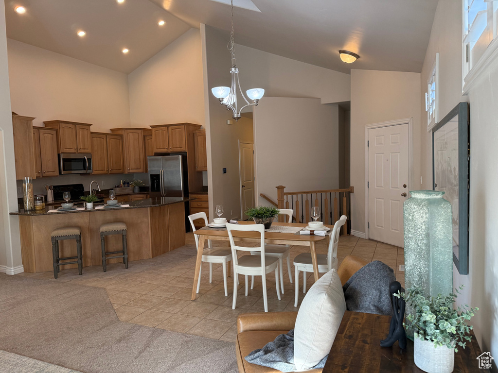 Dining area with high vaulted ceiling, light tile patterned floors, a chandelier, and baseboards