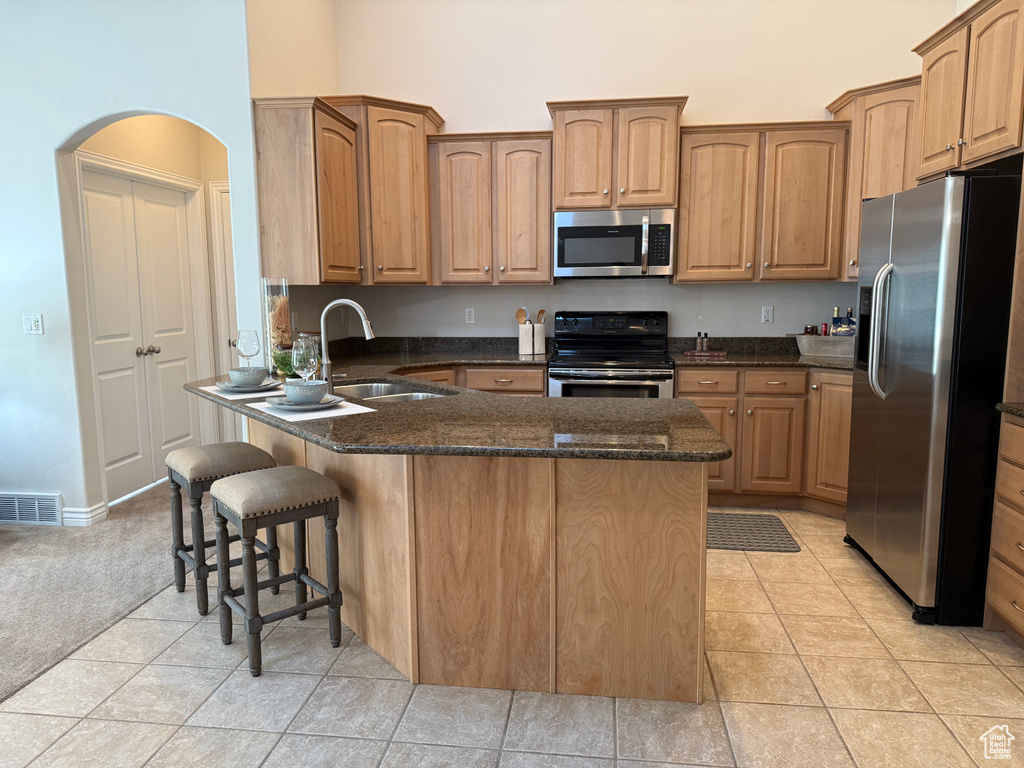 Kitchen with appliances with stainless steel finishes, a high ceiling, a breakfast bar area, a peninsula, and dark stone countertops