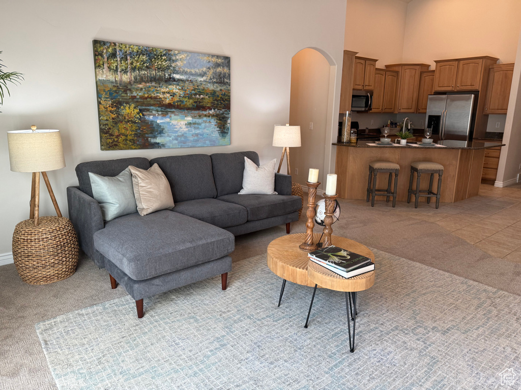 Living area featuring light colored carpet, arched walkways, baseboards, and a towering ceiling