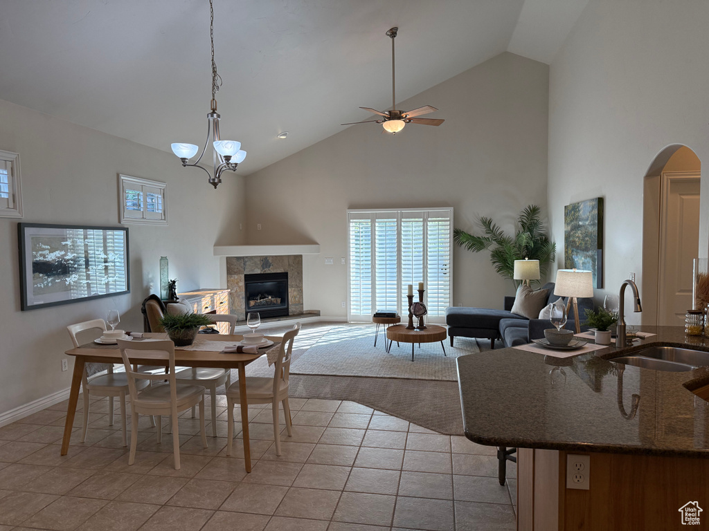 Living room with high vaulted ceiling, light tile patterned floors, a fireplace, arched walkways, and a ceiling fan