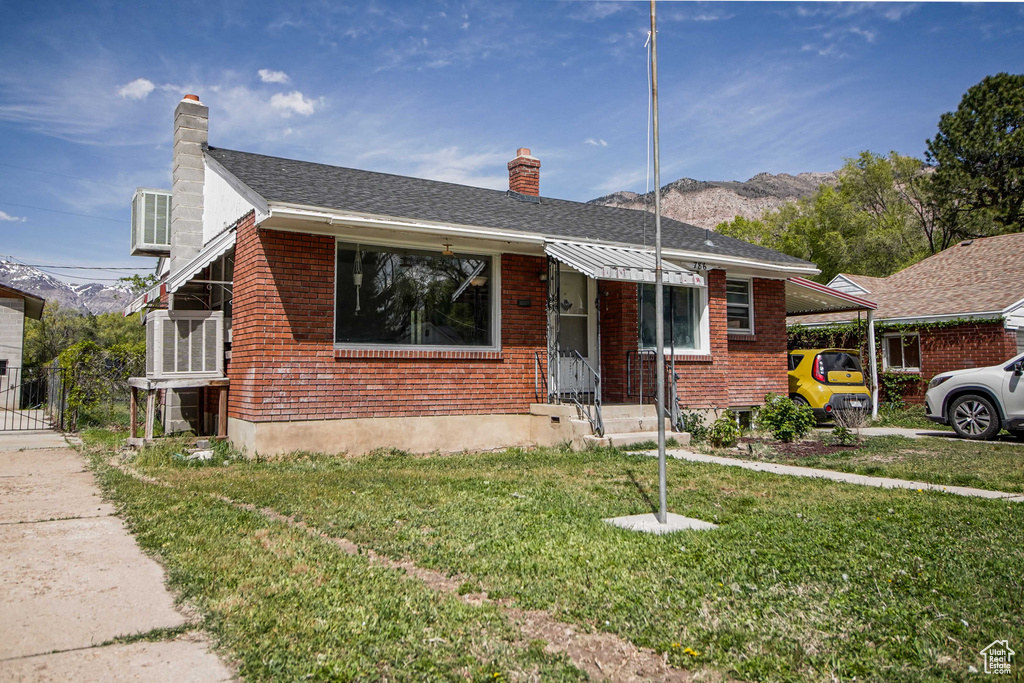 View of front of home with a chimney, brick siding, an attached carport, a mountain view, and a front lawn