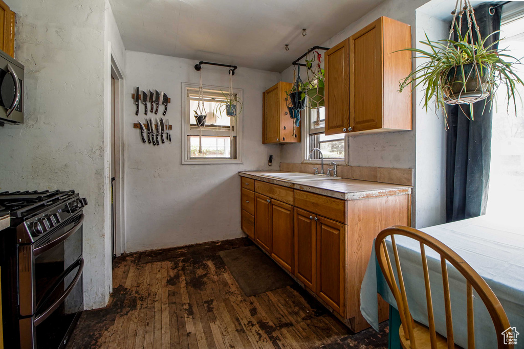 Kitchen featuring appliances with stainless steel finishes, light countertops, brown cabinets, a sink, and dark wood-type flooring