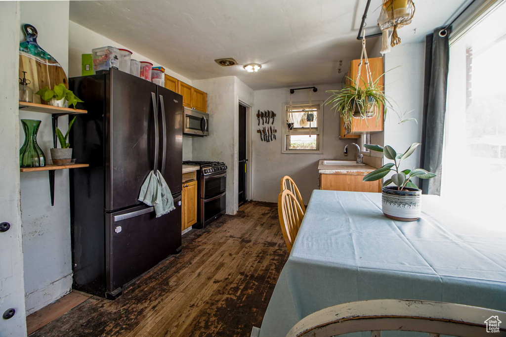 Kitchen with open shelves, stainless steel appliances, light countertops, dark wood-style flooring, and brown cabinetry