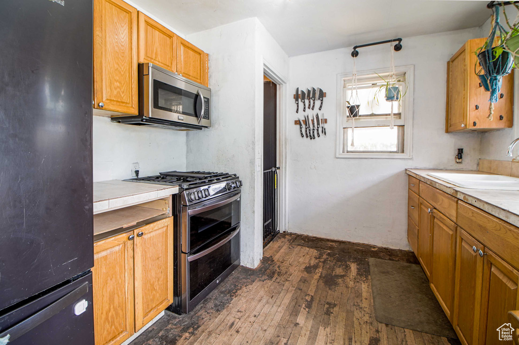 Kitchen with appliances with stainless steel finishes, dark wood-type flooring, light countertops, and a sink